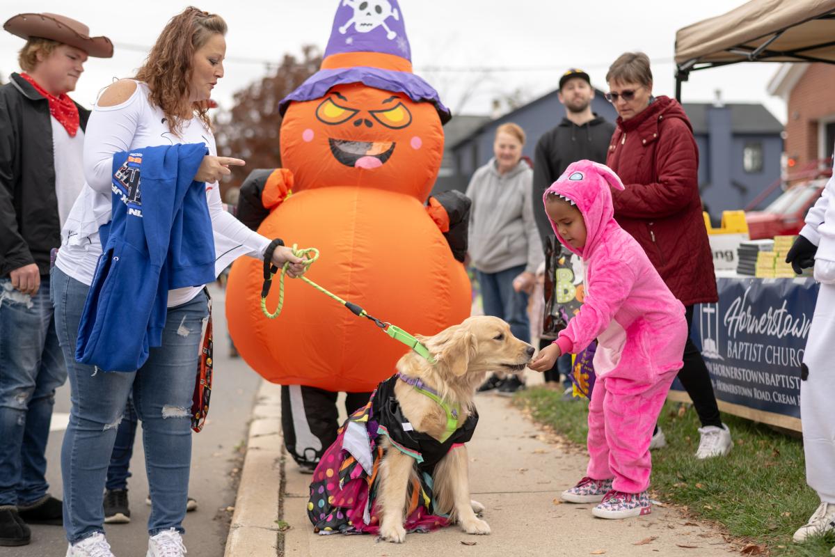 Dog getting a treat from a child dressed as a pink dinosaur