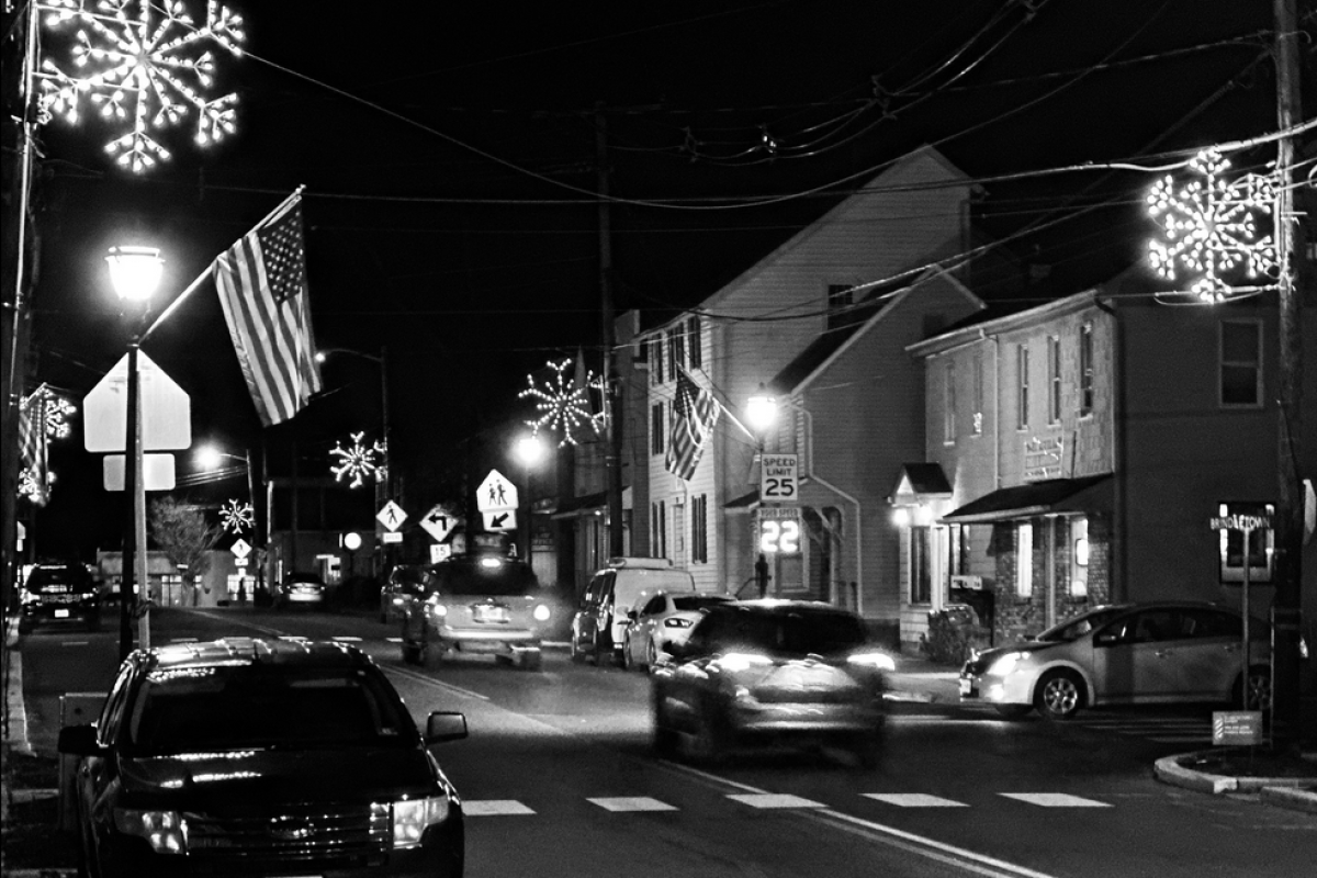 Black and white photo of Mainstreet with lit snowflakes on telephone poles.  Cars on the street and buildings in background