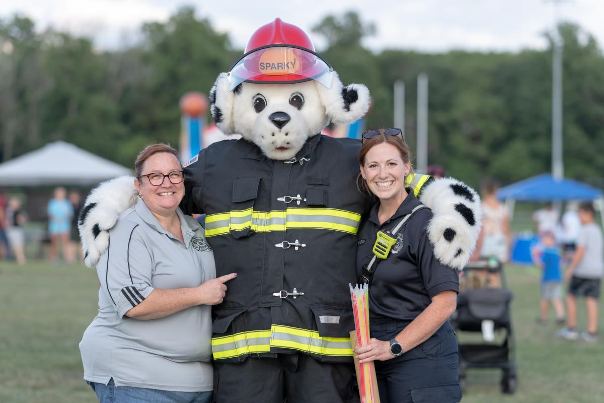 Person in Dalmation dog costure, in fireman gear, posing with two ladies from emergency services